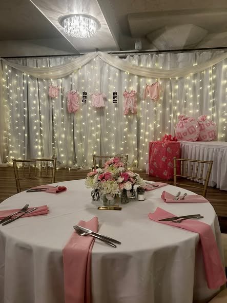 Round baby shower table with pink napkins and flowers in front of a light curtain
