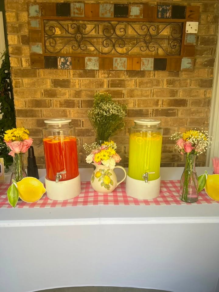 Pink and yellow lemonade in glass dispensers with flowers on a gingham table