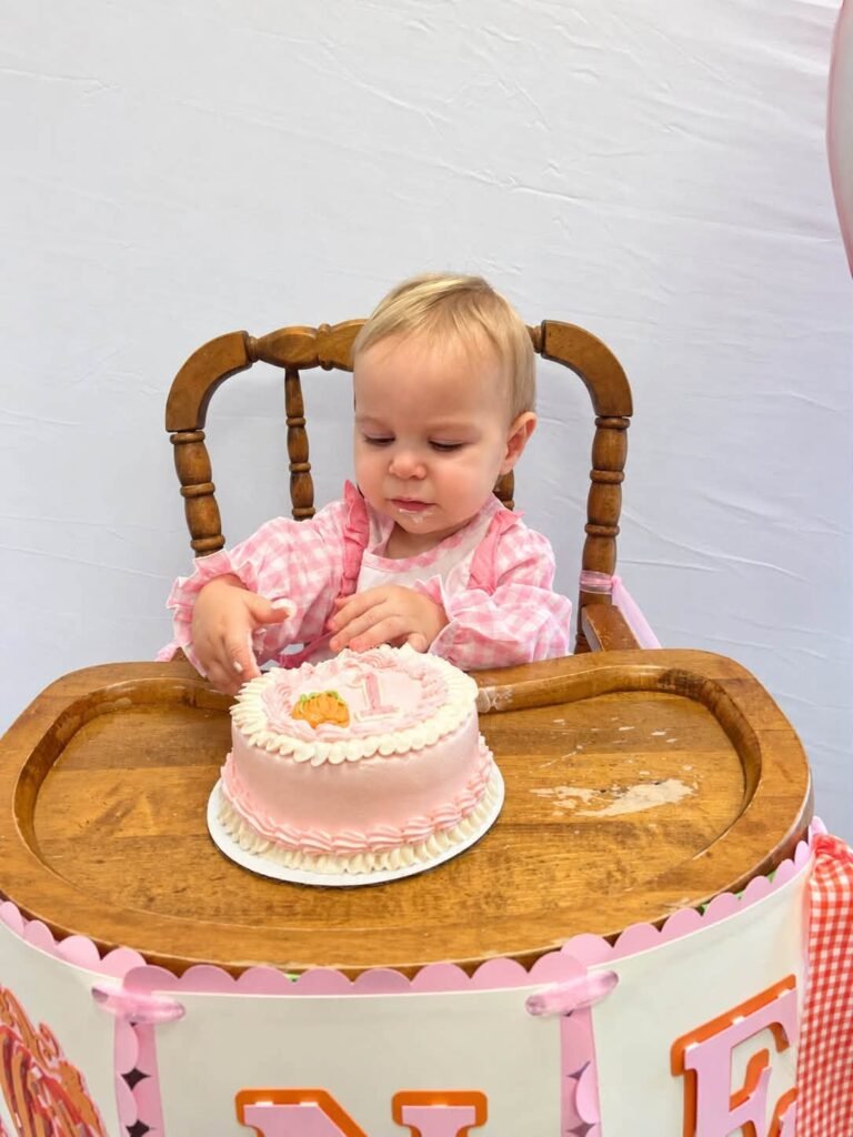 Baby girl with a pink smash cake on a wood high chair tray