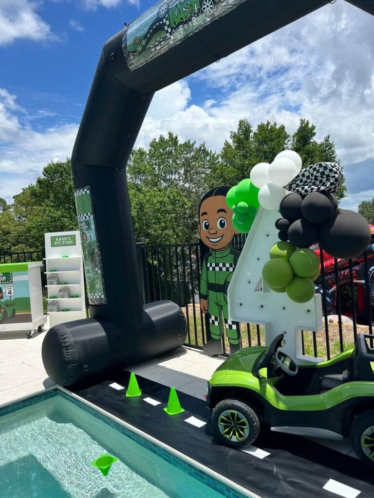 Inflatable finish line arch with a race car and checkered balloons by a pool