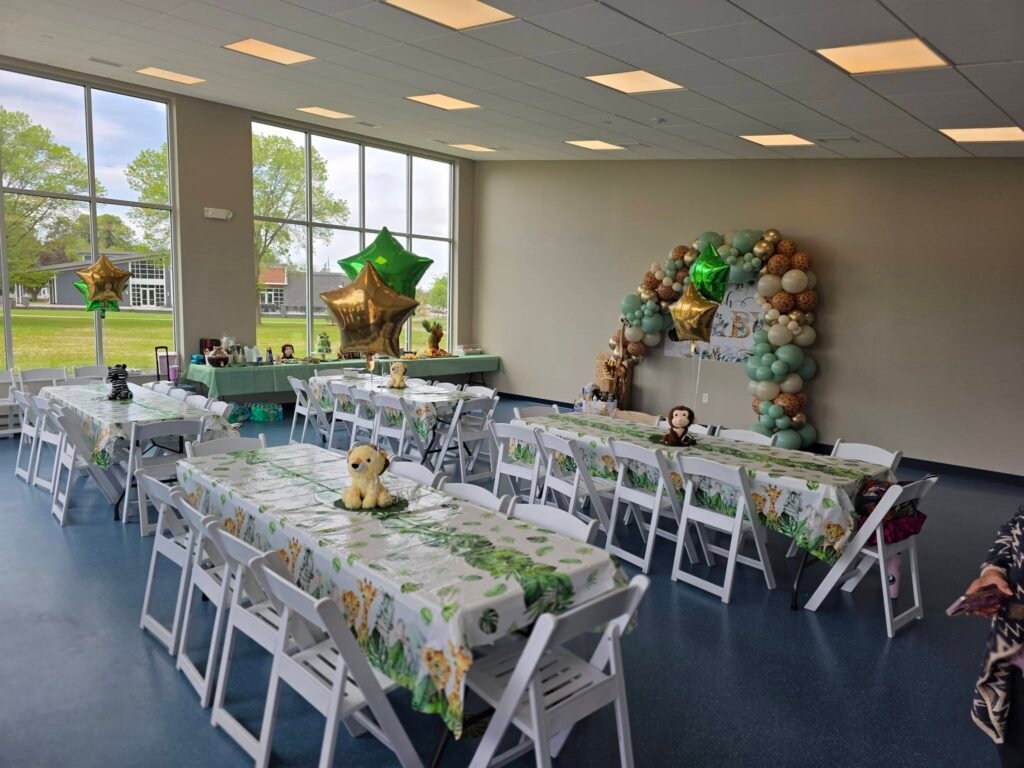 Baby shower hall with long tables, white chairs and a safari backdrop