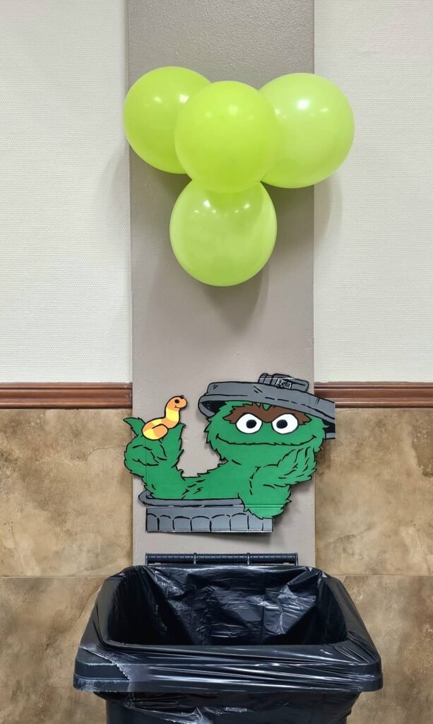 Trash can dressed as Oscar the Grouch with a green balloon cluster