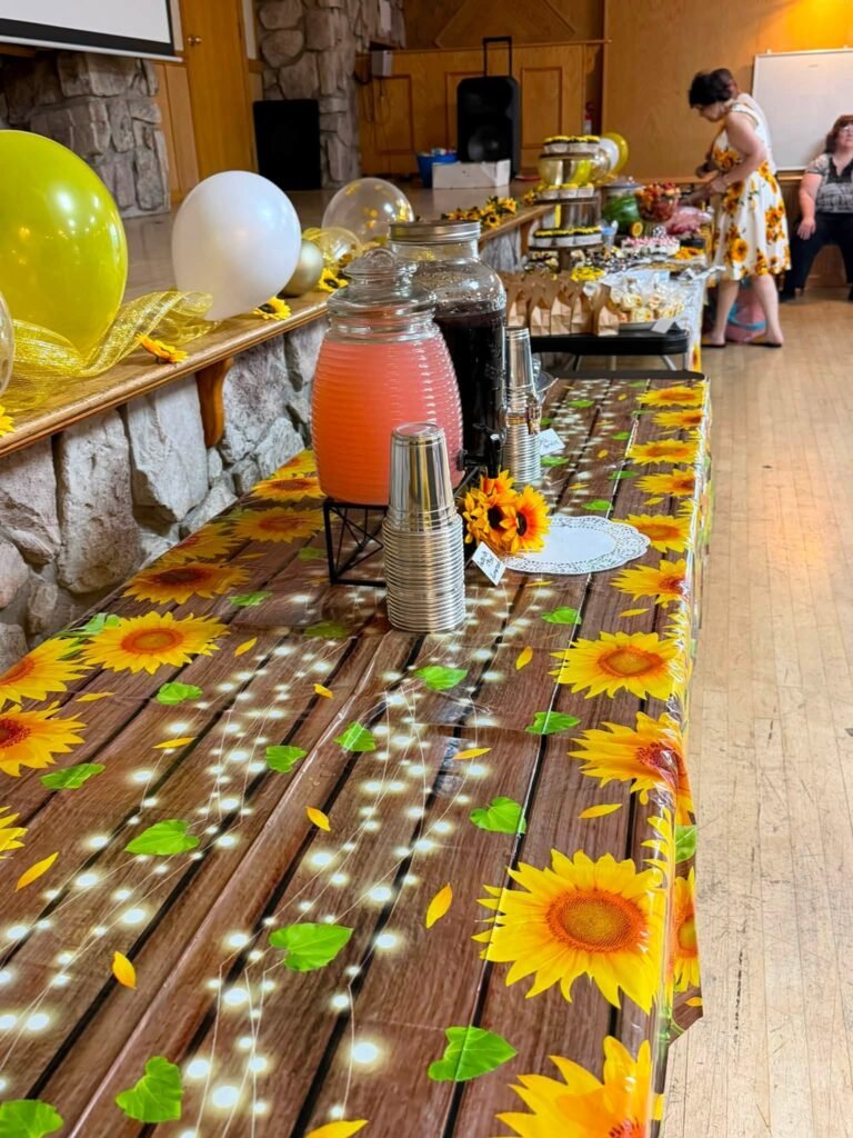 Long food table with a sunflower runner, pink drinks and balloons