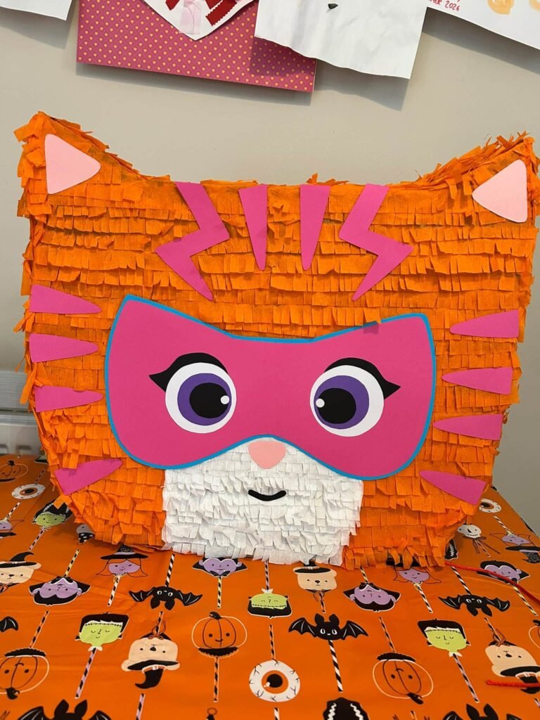 Orange and pink fringe pinata shaped like a super kitty