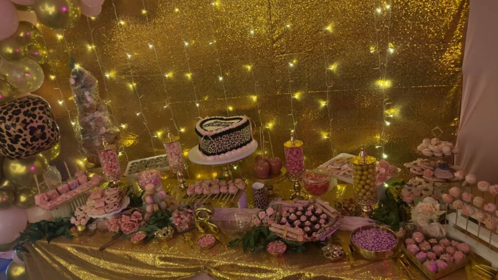 Dessert table in front of a gold sequin wall with fairy lights