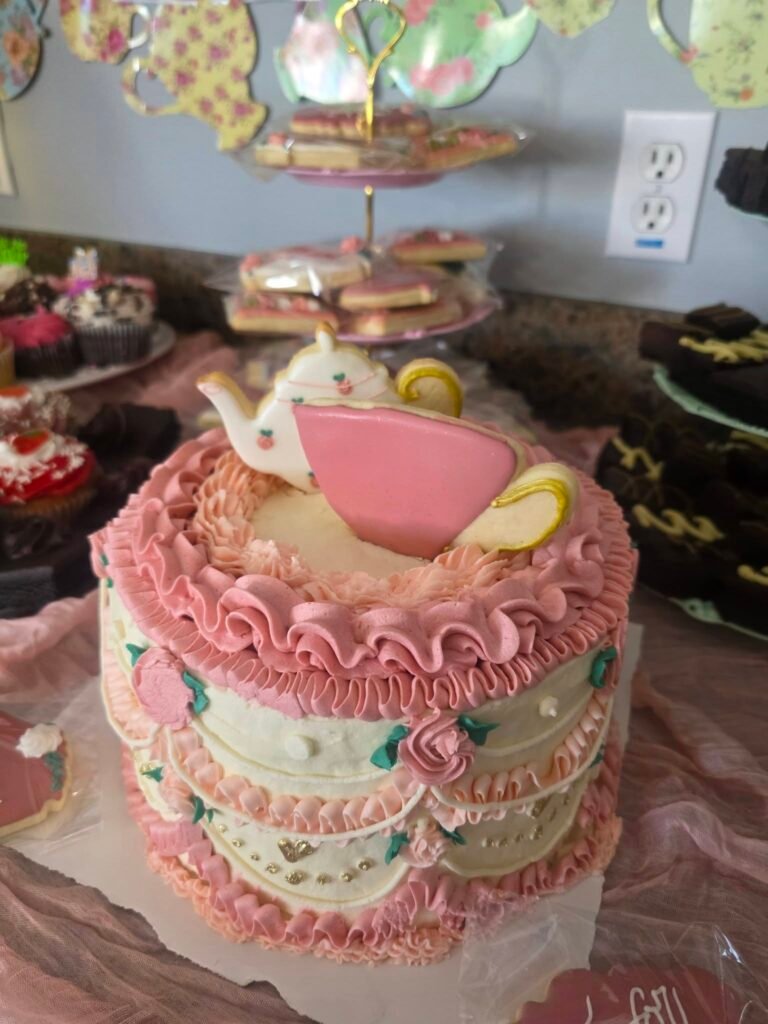 Pink birthday cake with a teapot topper and piped details