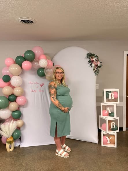 Mom to be in a sage green dress in front of a pink and sage balloon arch