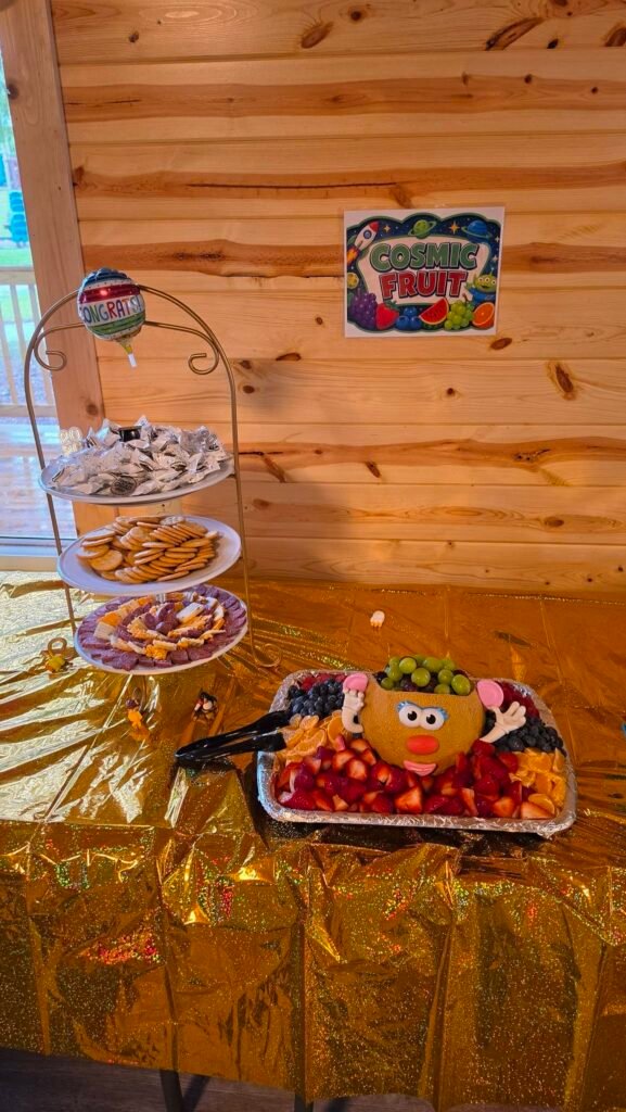 Graduation party table with a dessert stand and fruit tray on a gold cloth