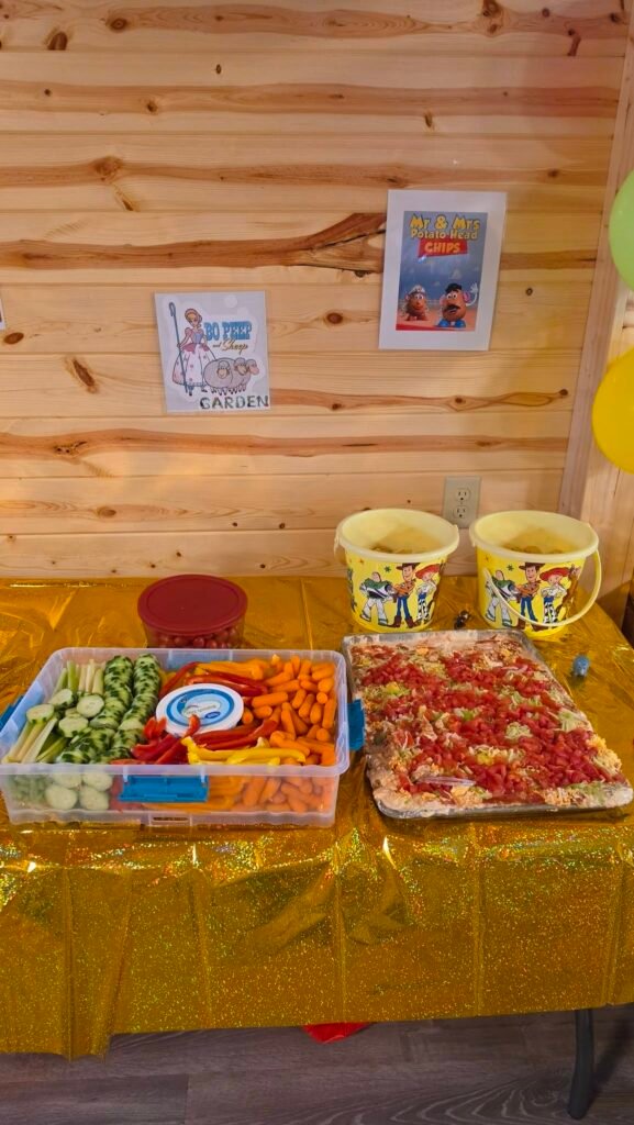 Snack table with a veggie tray, pizza and Toy Story signs