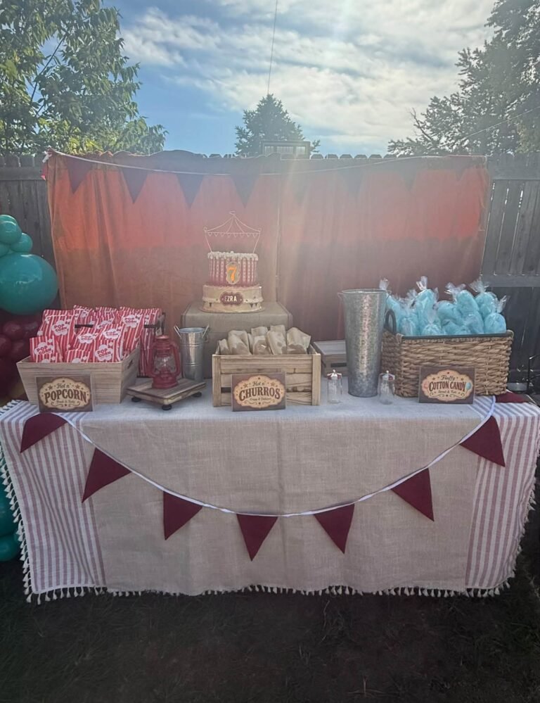 Carnival treat table with a striped cloth, red flag bunting, popcorn boxes and cotton candy bags