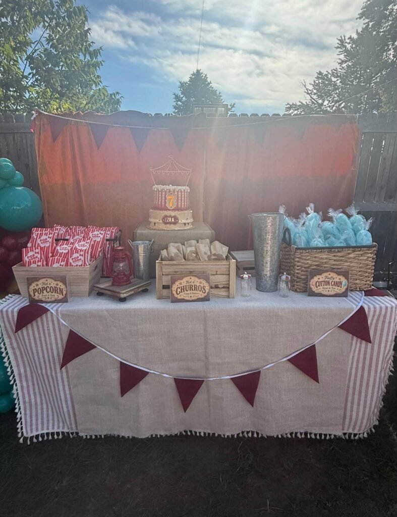 Carnival treat table with a striped cloth, red flag bunting, popcorn boxes and cotton candy bags