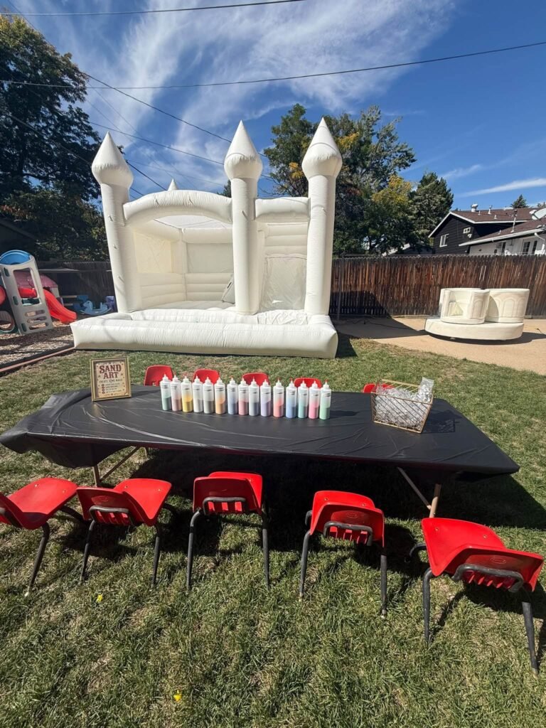 White bounce castle with a black kids table and red chairs on the grass