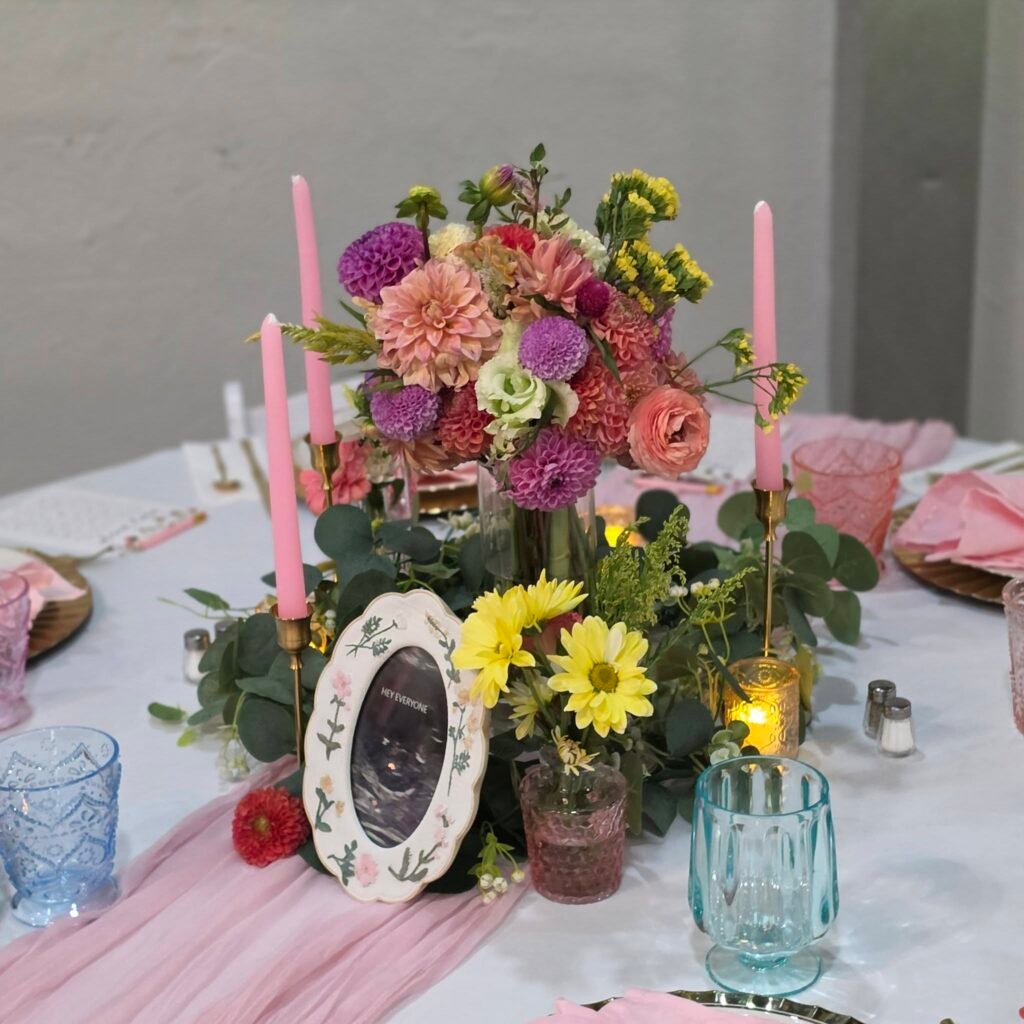 Wildflower centerpiece with pink candles and a framed photo on a round table