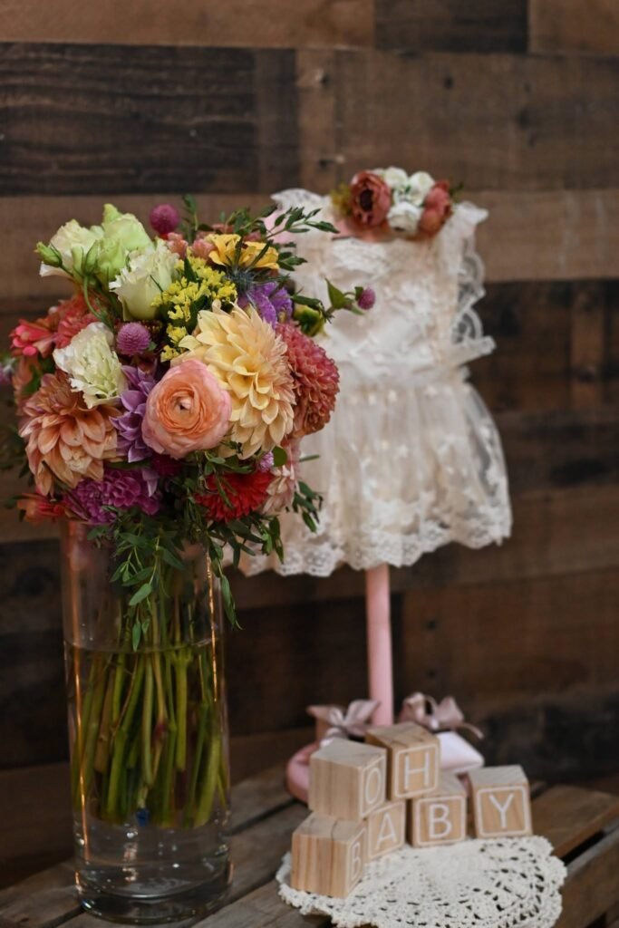 Mixed flower vase next to a tiny baby dress on a stand