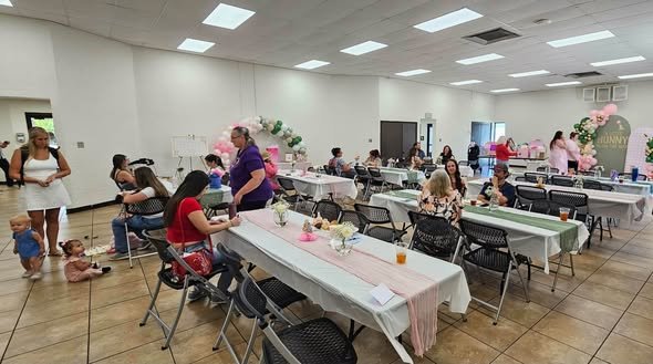 Baby shower hall with long tables and guests by a sage and pink backdrop