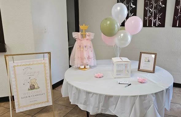 Tiny pink dress display with balloons and a framed sign at a baby shower