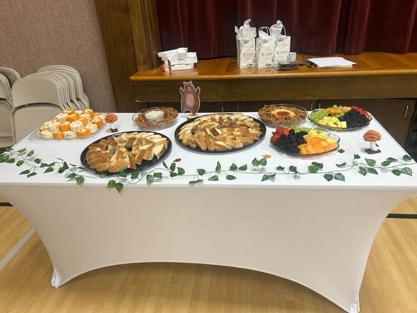Long baby shower food table with trays of food and an ivy garland