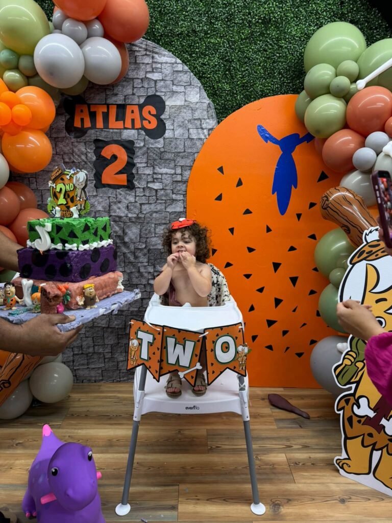 Stone backdrop with a balloon garland, high chair and Flintstones cake